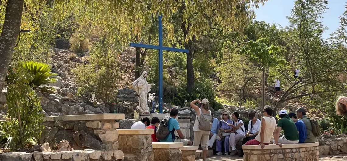 Pilgrims beside the Blue Cross and Our Lady’s statue at an Apparition Hill tour stop in Medjugorje