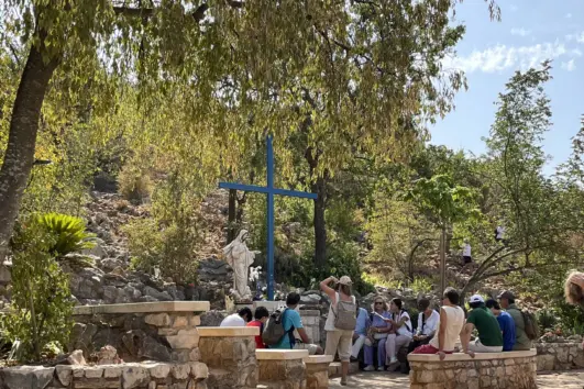 Pilgrims beside the Blue Cross and Our Lady’s statue at an Apparition Hill tour stop in Medjugorje