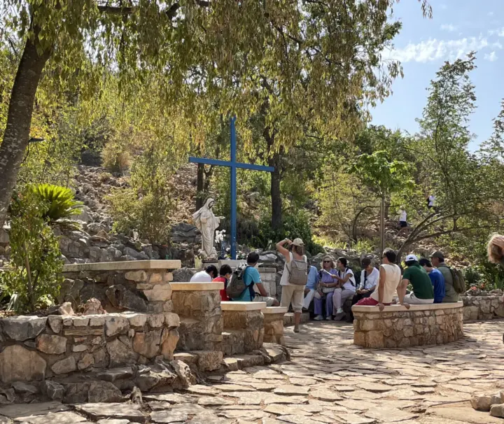Apparition Hill Tour – Medjugorje Visionaries, Rosary & Messages 2 Pilgrims beside the Blue Cross and Our Lady’s statue at an Apparition Hill tour stop in Medjugorje